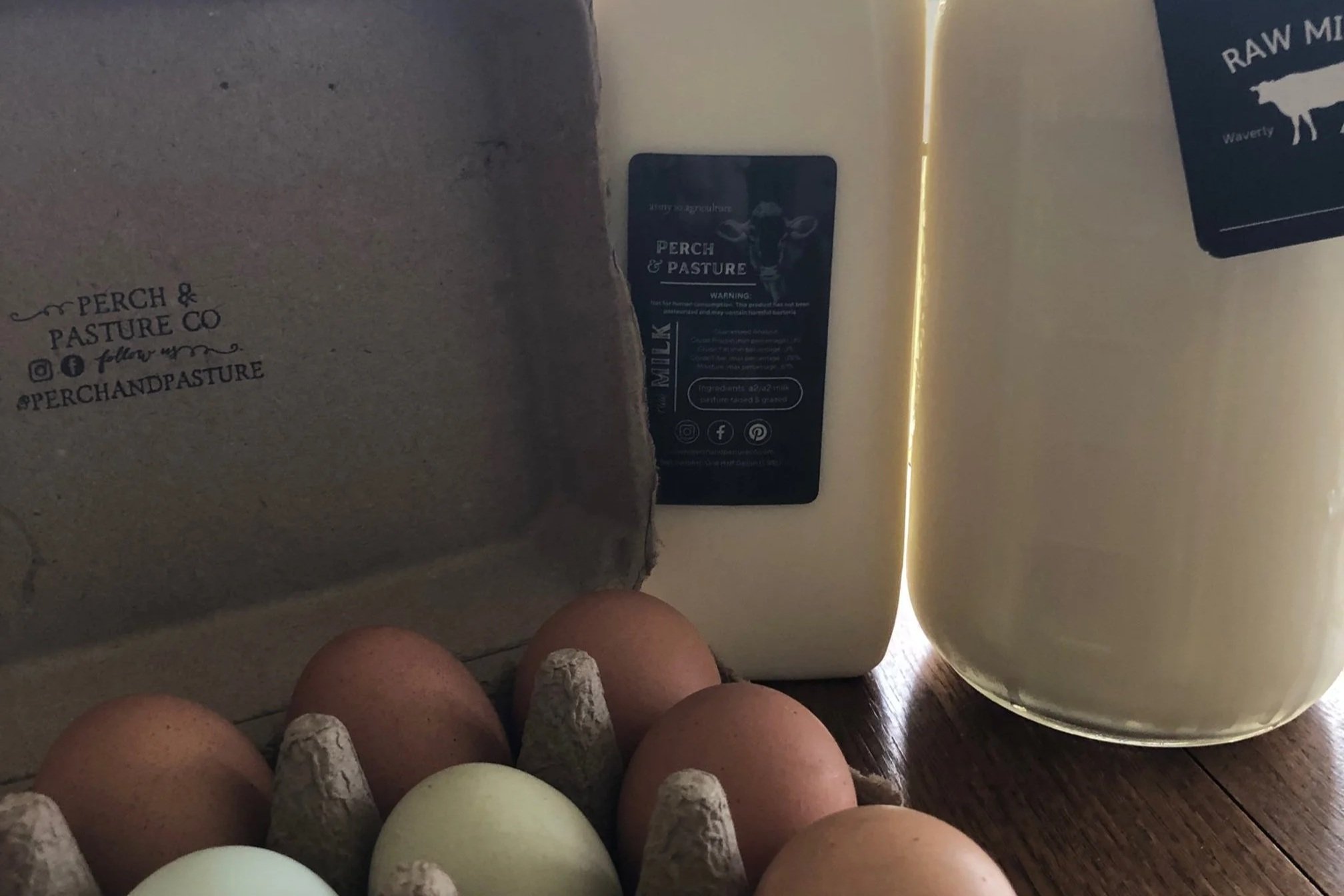 Farm-fresh eggs in a carton with a label from Perch & Pasture Co, alongside jars of raw milk, highlighting local dairy products and sustainable farming practices.